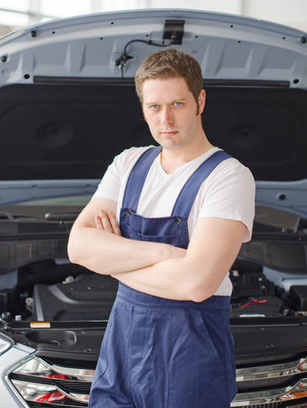 Young handsome mechanic standing near open car hood