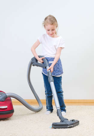 Cute little girl cleaning carpet with vacuum cleaner.の写真素材