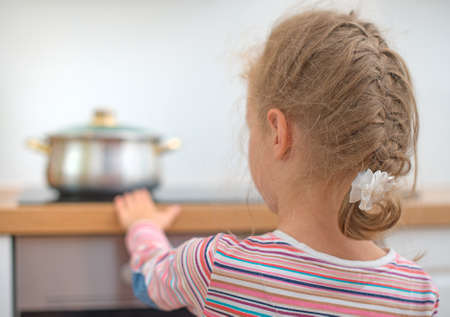 Little girl touches hot pan on the stove. Dangerous situation at home. の写真素材