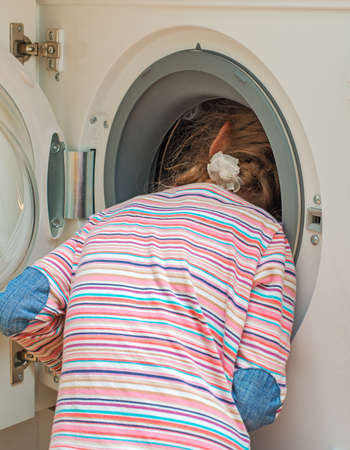 Little girl putting head into washing machine  Dangerous situation at home の写真素材