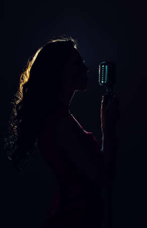 Silhouette of woman singing into vintage microphone.の写真素材