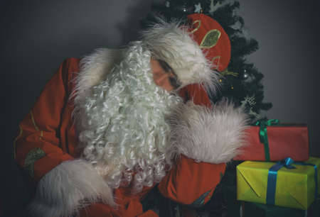 Santa Claus sleeping next to Christmas tree and gifts.の写真素材