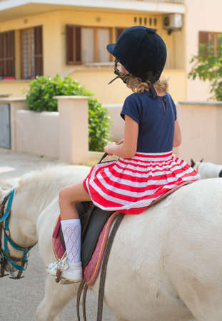 Portrait of little girl riding pony. From the back.の写真素材