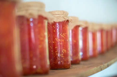Canned tomatoes in glass jars on wooden shelf.の写真素材
