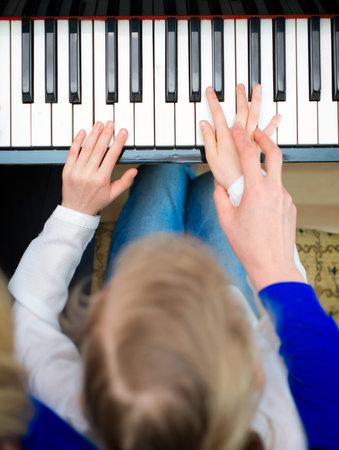 Woman teaching little girl to play the piano. Top view.