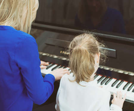 Woman teaching little girl to play the piano. Back view.の写真素材