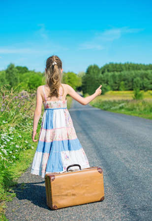 Little girl with vintage suitcase on rural road.の写真素材