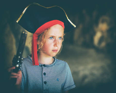 Little girl in pirate costume with musket gun near the cave entrance. Place for your text.の写真素材