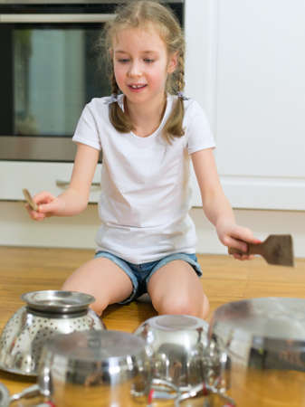 Little girl playing drums on pots and pans in the kitchen.の写真素材