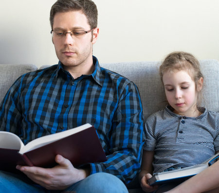 Father and his daughter reading books on sofa.