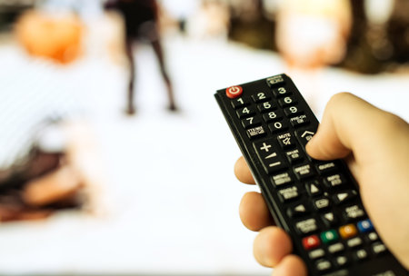 Male hand holding TV remote control.