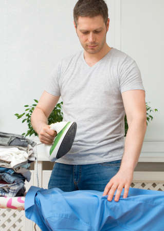 Handsome man ironing clothes on ironing board at home.の写真素材