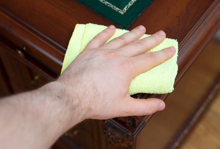 Man's hand wipes dust from antique furniture.