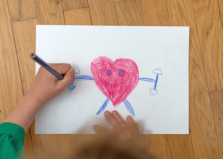 Child drawing funny sporty red heart on paper.