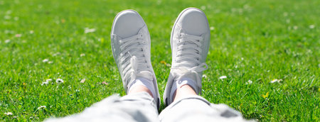 Legs in female sneakers on the grass.