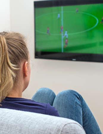 Woman watching football match on television at home.の写真素材