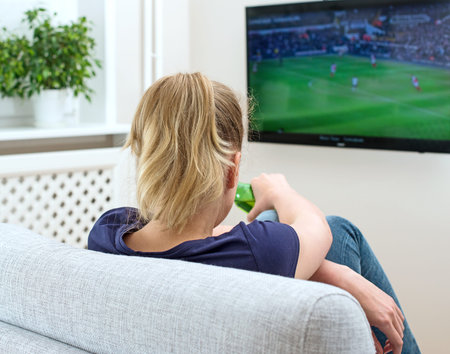 Woman watching football match on television at home.