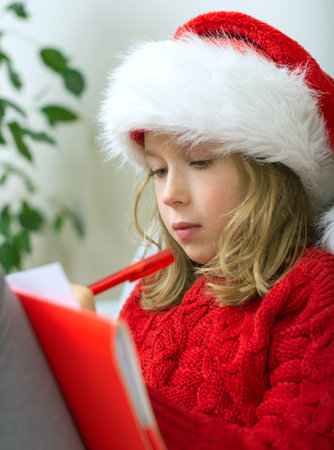 Little girl in red hat writing a letter to Santa Claus.の写真素材