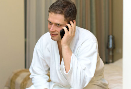 Man in bathrobe with mobile phone in hotel room.の写真素材
