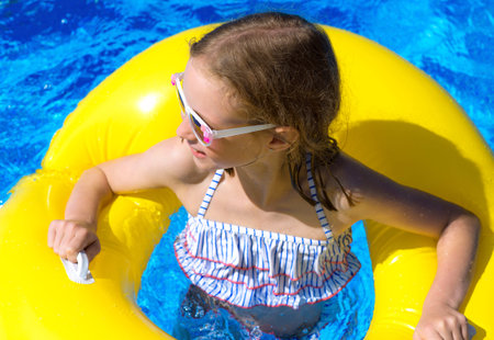 Portrait of little girl with inflatable rubber ring in swimming pool.