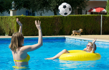 Little girl with her mom playing ball in swimming pool.