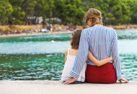 Little girl with mother sitting on the pier.の写真素材