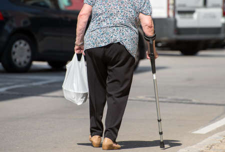 Elderly woman with crutch on the street.の写真素材