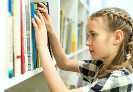Pretty little girl looking for a book in library.の写真素材