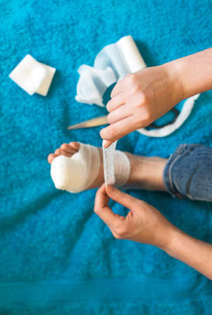 Woman bandaging her injured leg on sofa at home.の写真素材