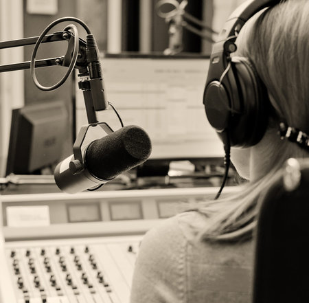 Rear view of female dj working in front of a microphone on the radio