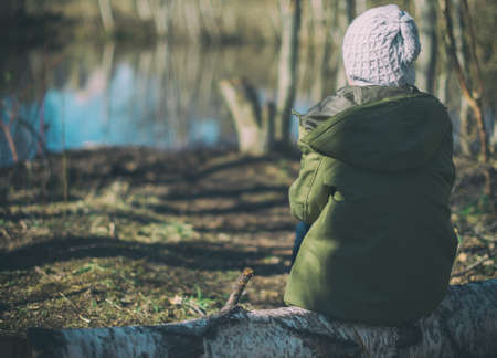 Little girl sitting on a log in the forest.の写真素材