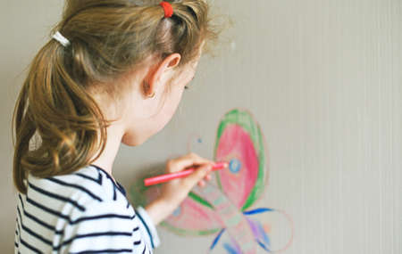 Little girl drawing on the wallpaper with pencil.の写真素材