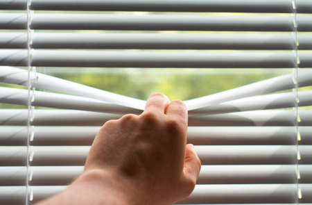 Man's hand revealing white venetian blinds.の写真素材