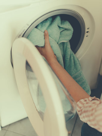 House cleaning. Woman putting towel in washing machine.
