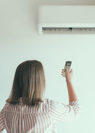 Woman holding remote control aimed at the air conditioner.の写真素材