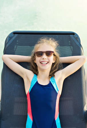 Little girl sunbathing on lounger near the water pool.の写真素材