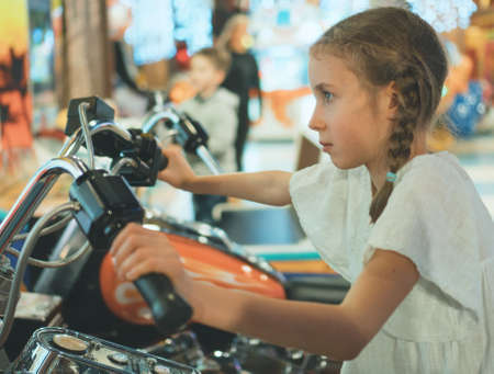 Little girl playing motorbike simulator game in theme park.の写真素材