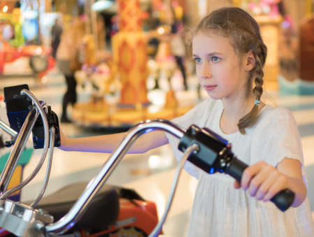 Little girl playing motorbike simulator game in theme park.の写真素材