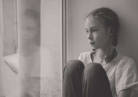 Sad little girl sitting near the window. Black and white.の写真素材