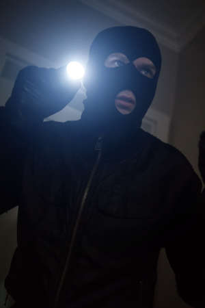 Thief wearing mask with a flashlight in the house.の写真素材