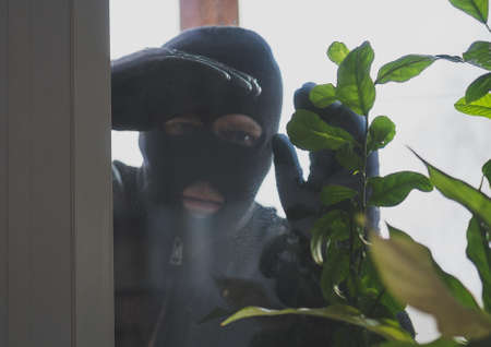 Thief in the mask looks through the window into the house.の写真素材