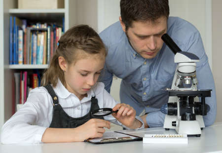 Little girl with teacher in science class with microscope on the table.の写真素材