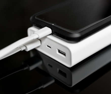 White power bank with smartphone on mirrored surface.の写真素材