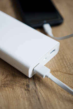 White power bank with smartphone on wooden surface.の写真素材