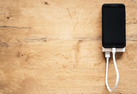 White power bank with smartphone on wooden surface. Space for your text.の写真素材