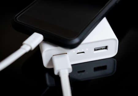 White power bank with smartphone on mirrored surface.の写真素材