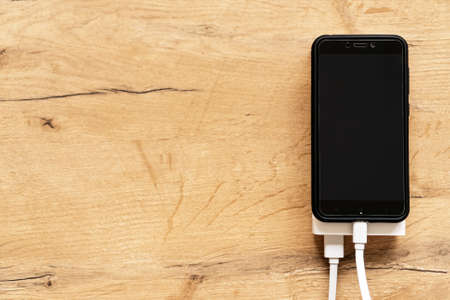 White power bank with smartphone on wooden surface. Space for your text.の写真素材