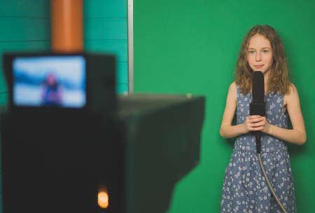 Little girl with microphone standing in front of camera on green screen.の写真素材
