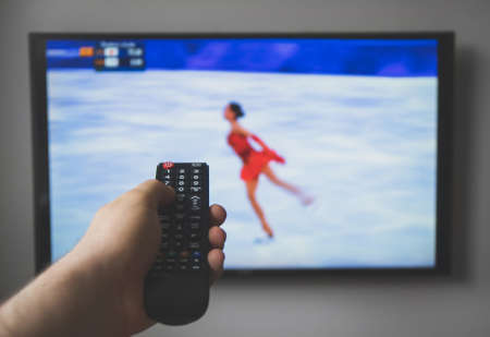 Male hand holding TV remote control. Figure skating.の写真素材