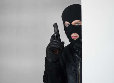 Armed man in balaclava hiding behind a wall.の写真素材